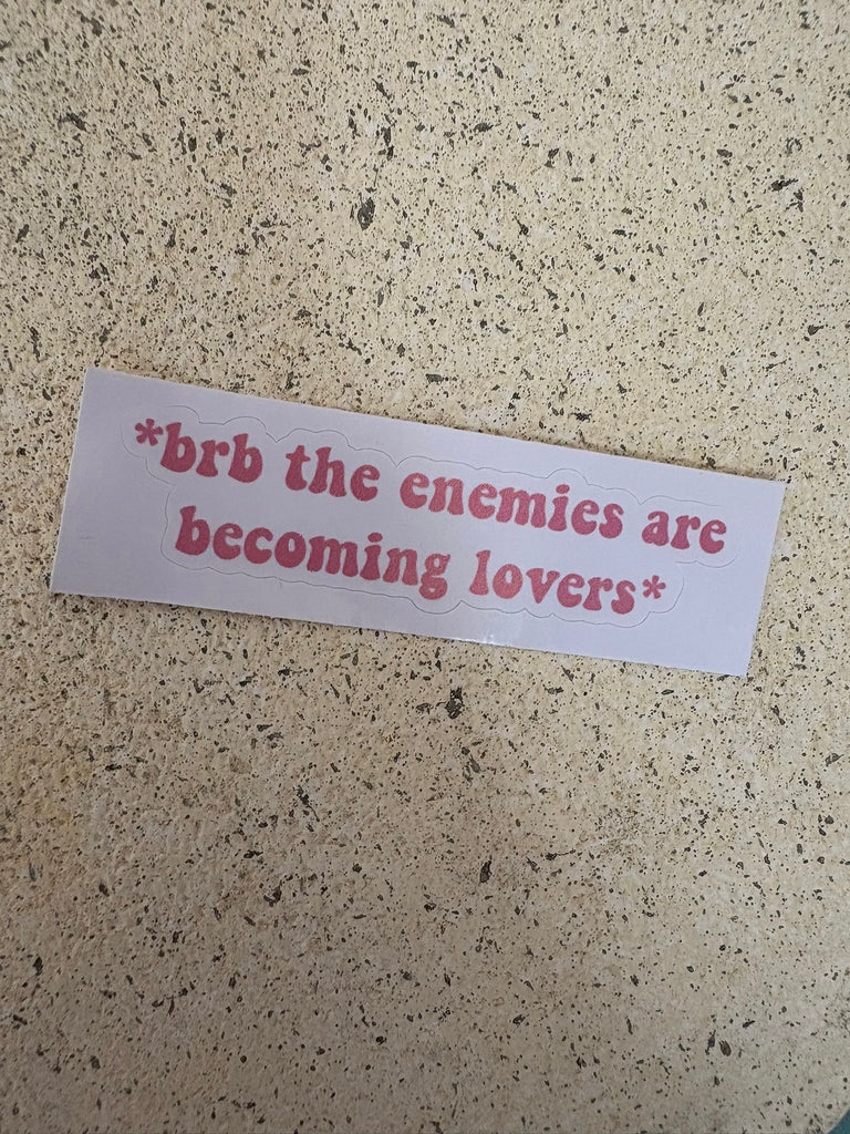 Pink text sticker reading “brb the enemies are becoming lovers.”