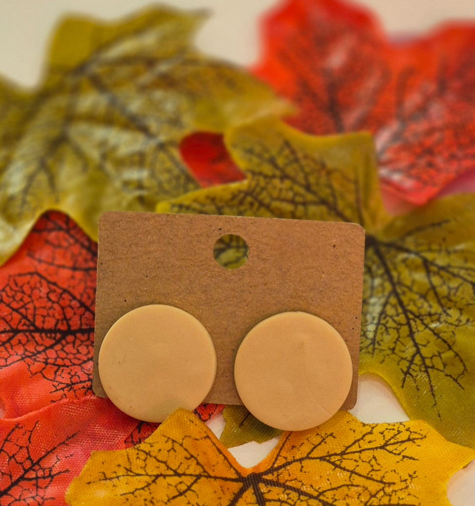 Beige round polymer clay stud earrings displayed on a brown backing card surrounded by autumn leaves in yellow, orange, and red tones.