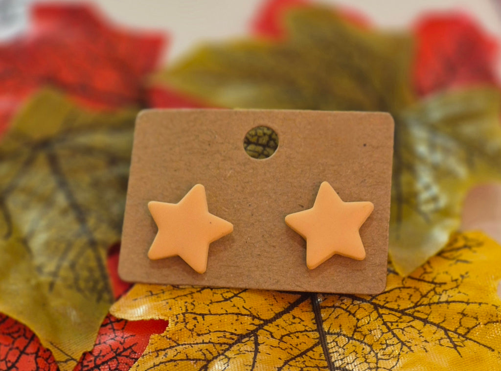 Peach star-shaped polymer clay stud earrings displayed on a brown backing card surrounded by autumn leaves in yellow, red, and green tones.