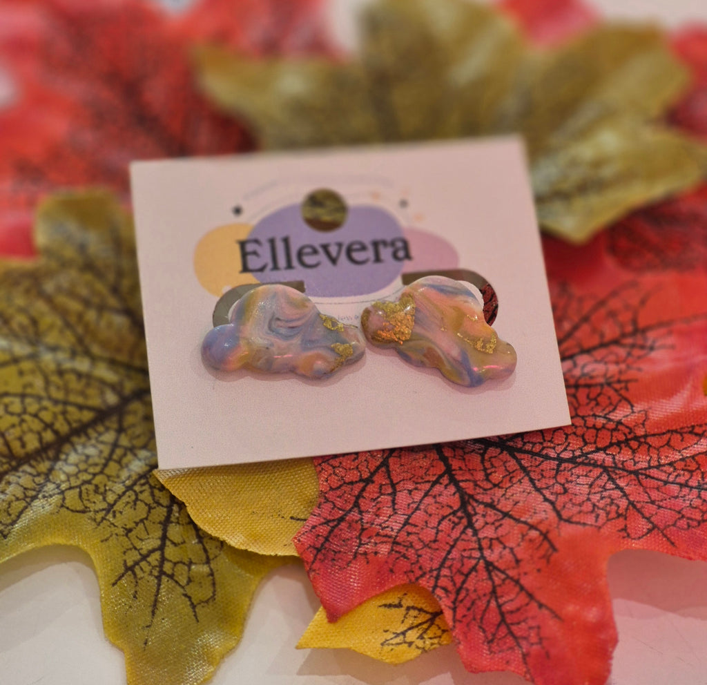 Pastel iridescent polymer clay cloud stud earrings with gold leaf detailing, displayed on an Ellevera jewellery card surrounded by autumn leaves.