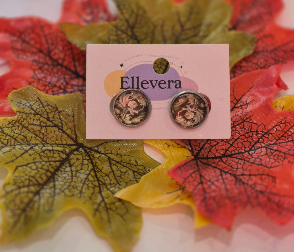Silver-toned glass stud earrings with vintage floral designs, displayed on a pink Ellevera card surrounded by colourful autumn leaves.