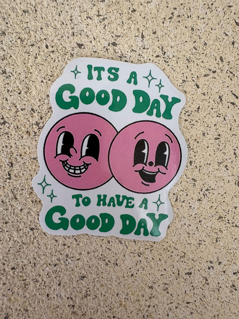 Retro-style sticker with pink faces and text “It’s a good day to have a good day.”