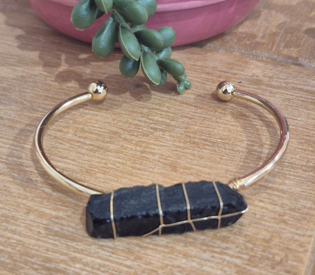 Gold cuff bracelet with raw black tourmaline crystal wrapped in gold wire.