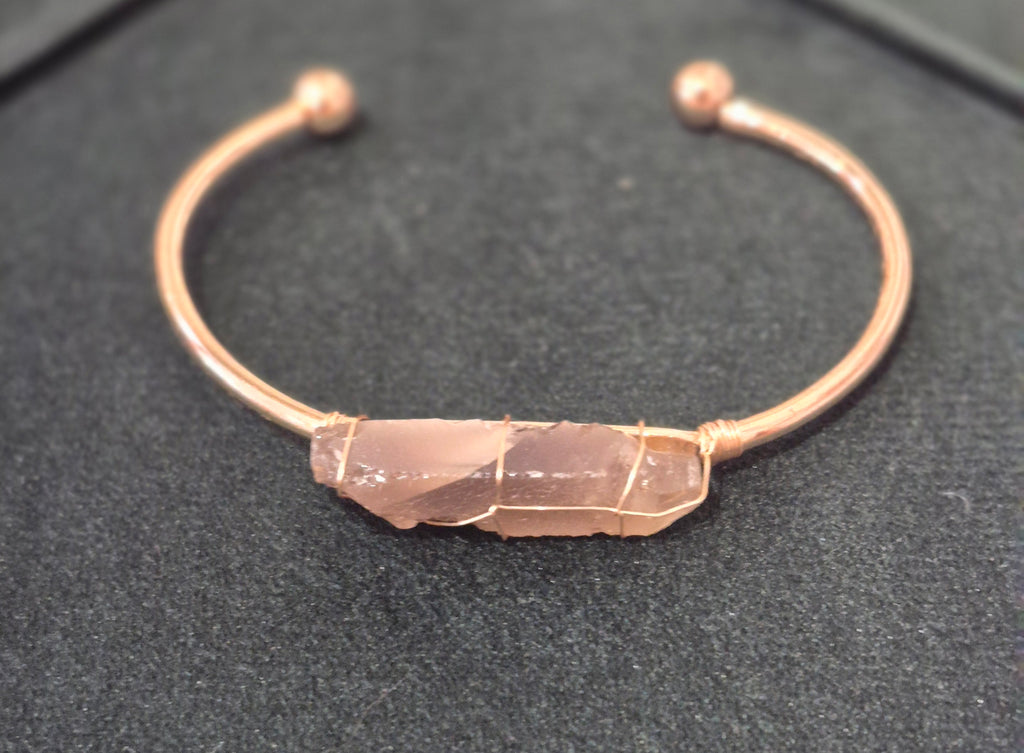 Gold adjustable cuff bracelet featuring a raw smokey quartz crystal wrapped in wire, displayed on a black background.