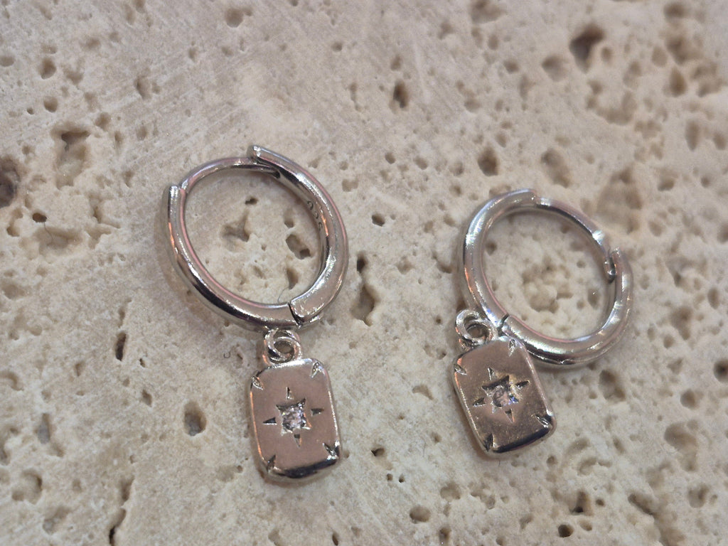 Silver North Star engraved huggy hoop earrings displayed on a textured stone background.