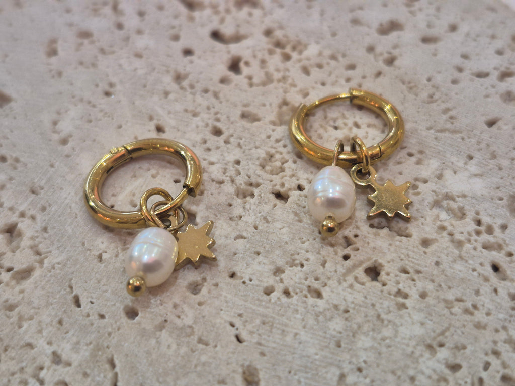 Gold-plated huggy hoop earrings with pearl and star charms displayed on a textured stone background.