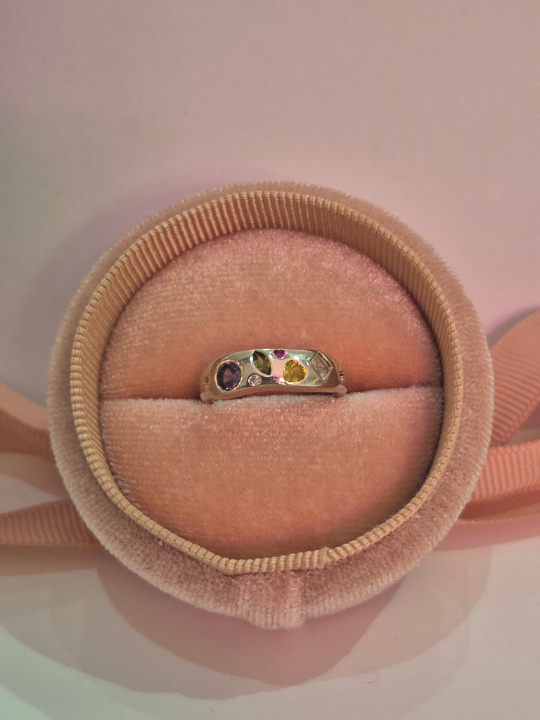 Silver ring with multicoloured gemstones displayed in a soft pink velvet ring box.