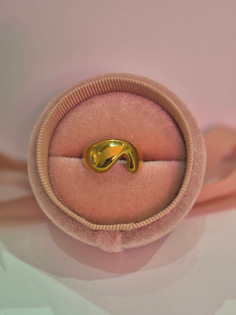 Gold molten wave ring displayed in a pink velvet ring box with soft lighting.