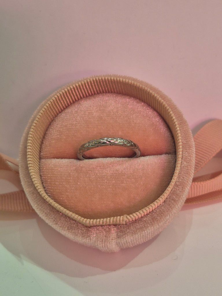 Silver braided band ring displayed in a pink velvet ring box with soft pink lighting.