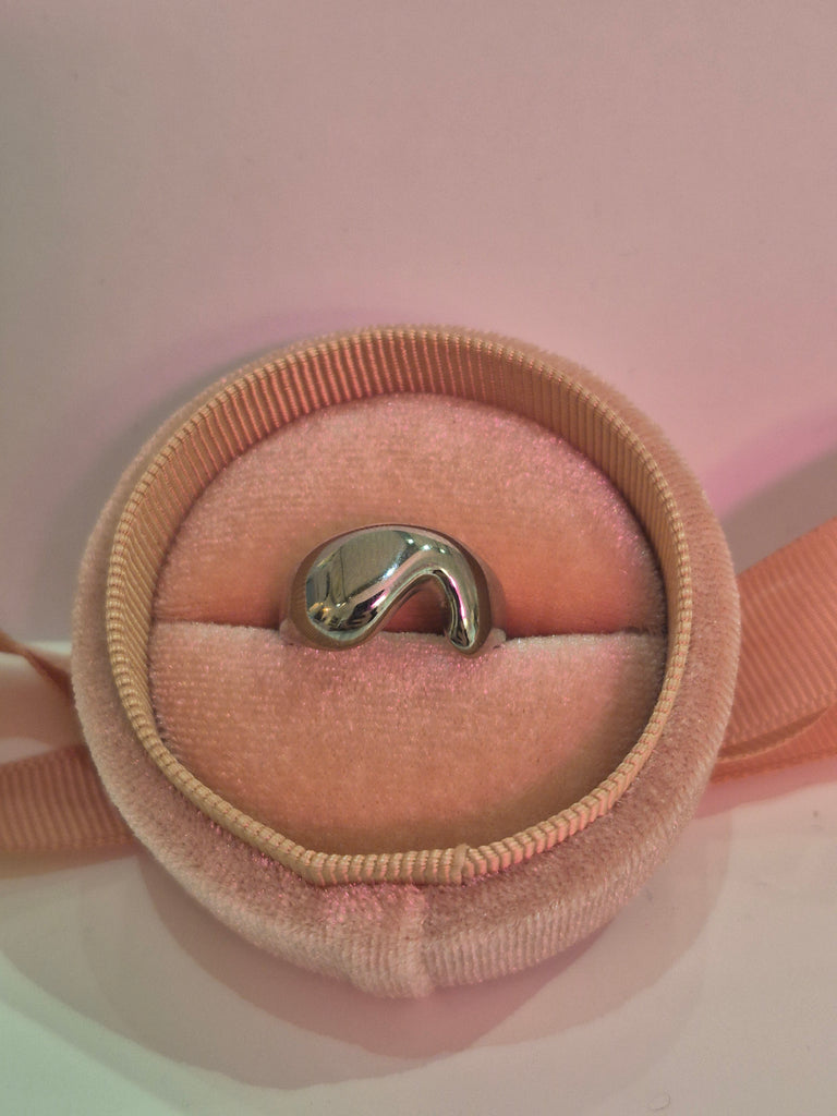 Silver molten wave ring displayed in a soft pink velvet ring box with gentle lighting.