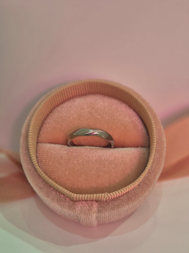 Silver twisted band ring displayed in a pink velvet ring box with soft lighting.