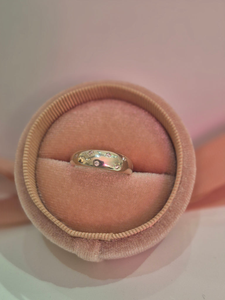 Silver ring with engraved stars and tiny clear stones displayed in a pink velvet ring box.