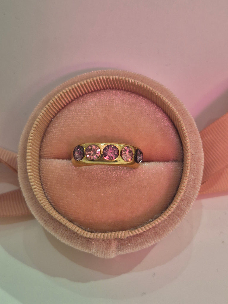 Gold ring with five pink and purple gemstones displayed in a blush velvet ring box.