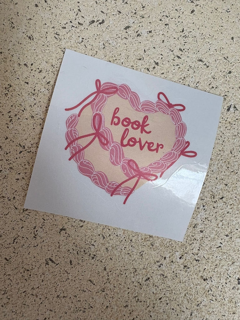 Heart-shaped ribbon design sticker with text “Book Lover.”