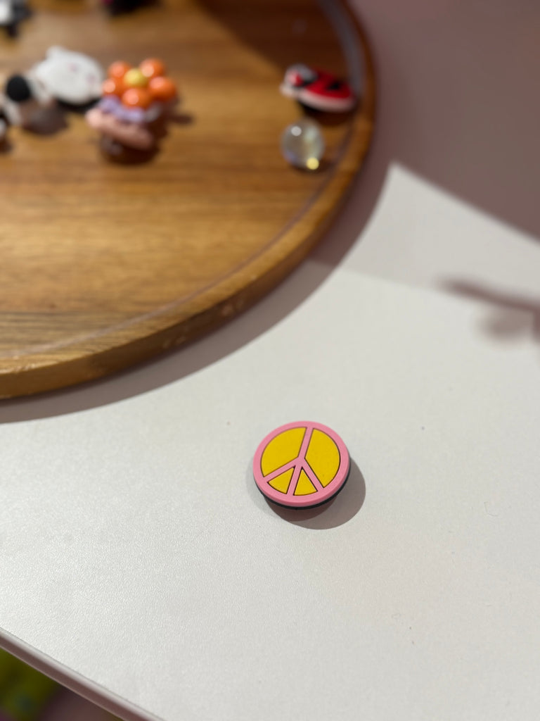 Pink and yellow peace sign Croc charm on white background.