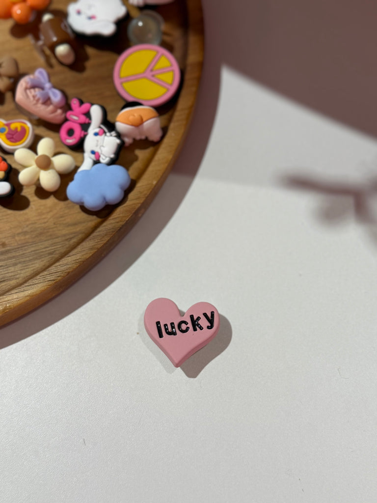 Pink heart Croc charm with “lucky” text.