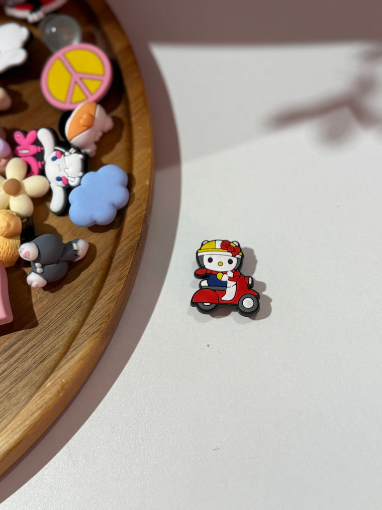 Croc charm of a kitty character riding a red scooter.