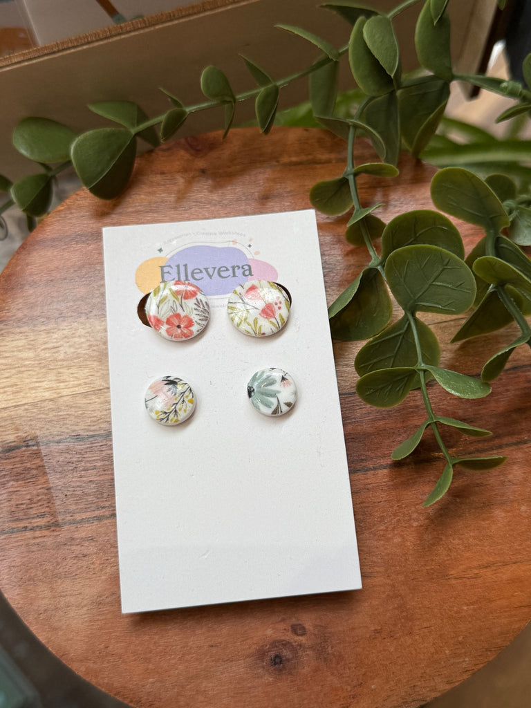 Two pairs of handmade floral polymer clay stud earrings in pastel botanical designs, displayed on Ellevera backing card.