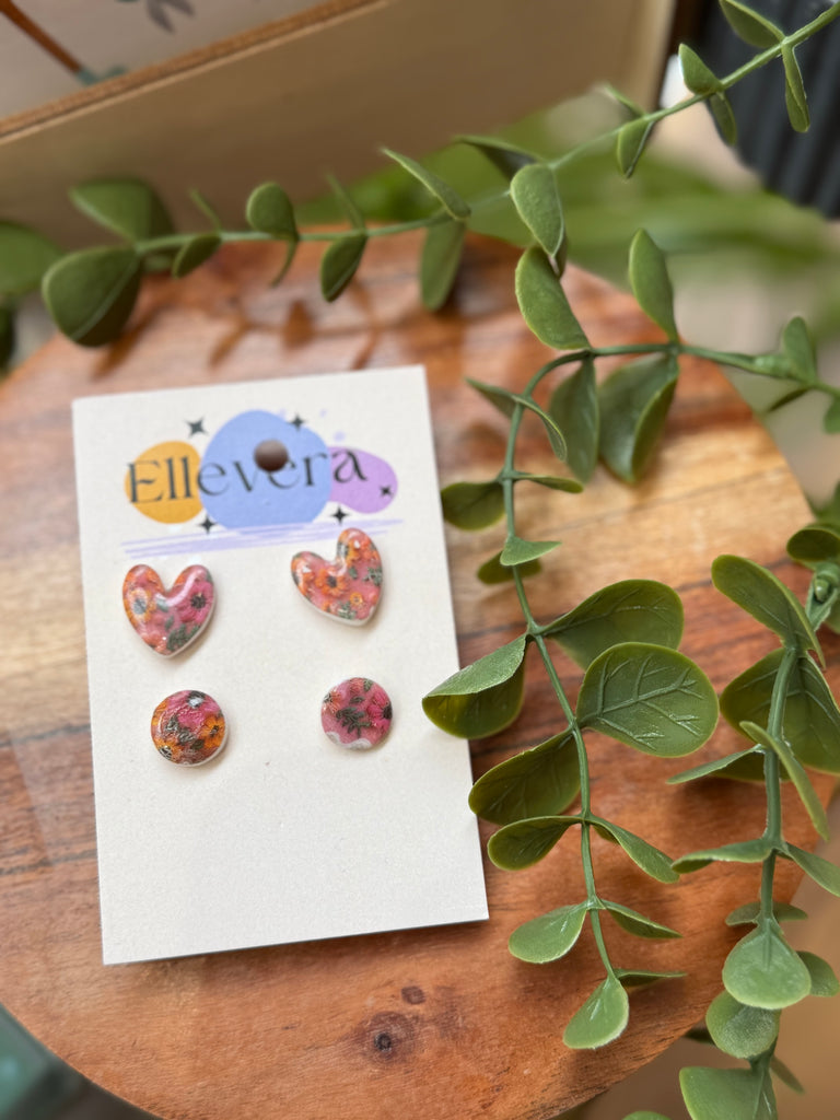 Set of two handmade polymer clay stud earrings featuring floral prints in heart and circle shapes, displayed on Ellevera backing card.