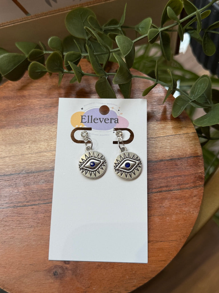 Silver drop earrings with engraved evil eye design and blue enamel detail.