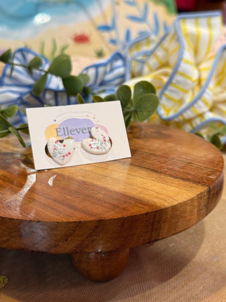 White heart-shaped polymer clay earrings with floral design on Ellevera backing card.
