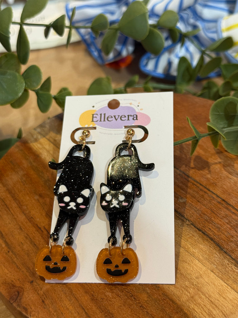 Black cat acrylic earrings holding orange pumpkins on Ellevera backing card.