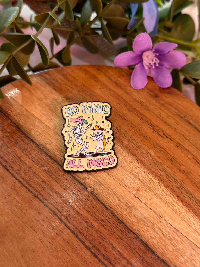 Enamel pin with skeletons dancing in disco hats and text “No Panic All Disco.”