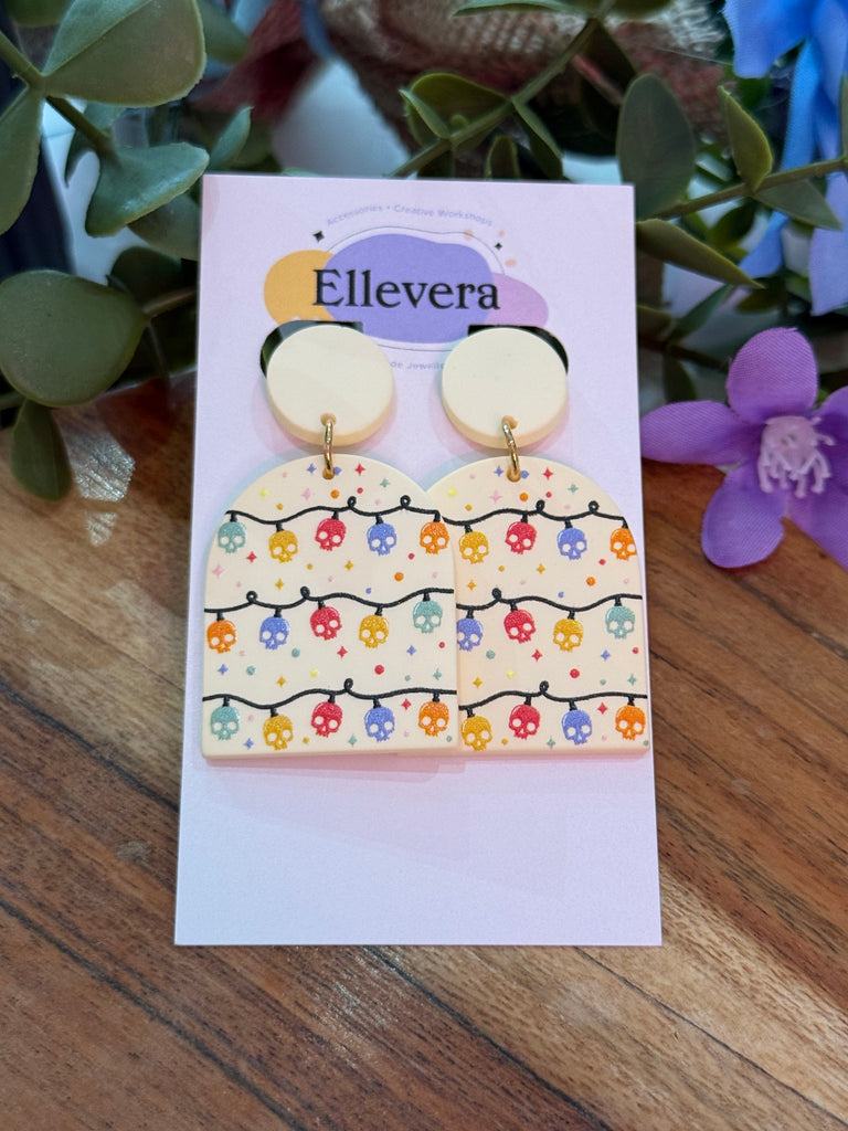 Rainbow skull string statement earrings with multicoloured skull fairy light design on a cream background, displayed on Ellevera backing card.