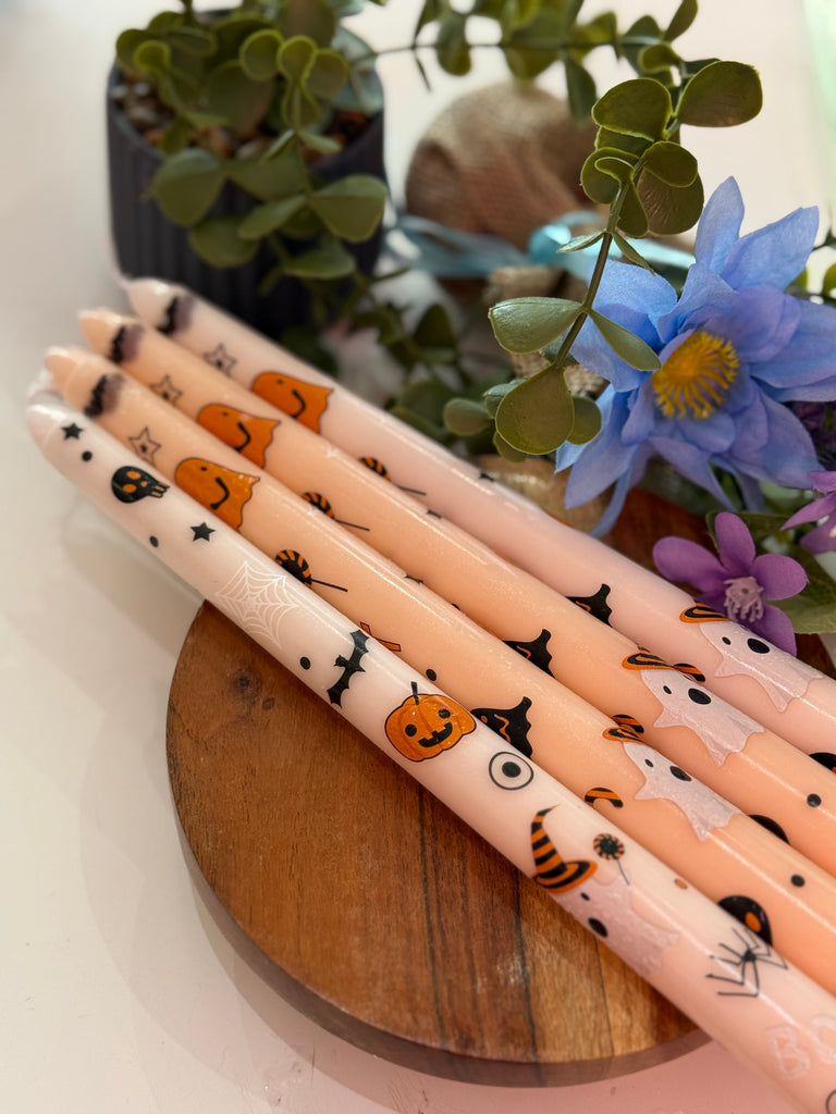 “Set of four taper candles decorated with Halloween-themed prints including pumpkins, bats, and ghosts.”