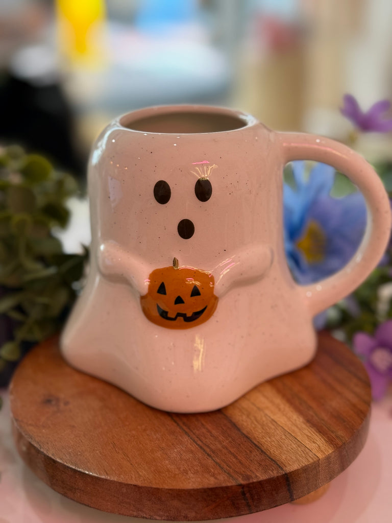 White ceramic ghost-shaped mug holding a small pumpkin design, styled with flowers and plants