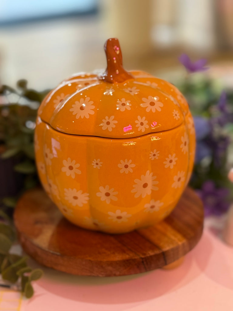 Orange pumpkin-shaped oil and wax melt burner with white daisy designs, placed on a wooden display stand.