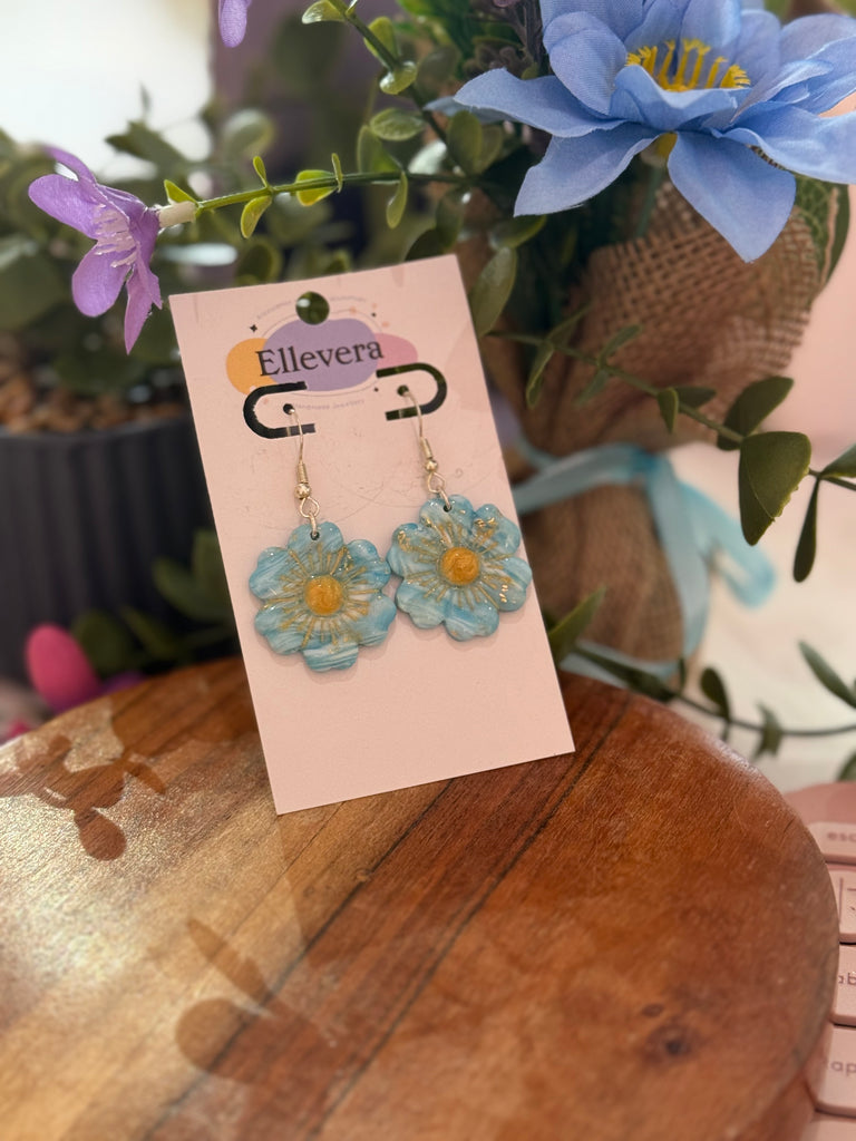 Handmade blue daisy flower polymer clay earrings with golden centres on Ellevera backing card.