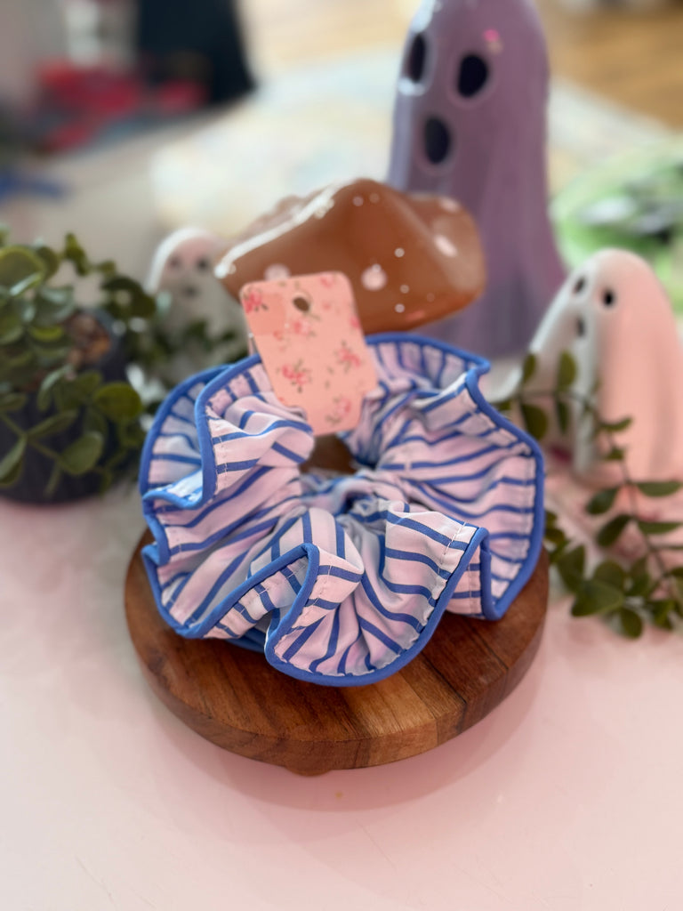 Blue and white striped ruffle scrunchie with bold blue trim displayed on wooden stand.