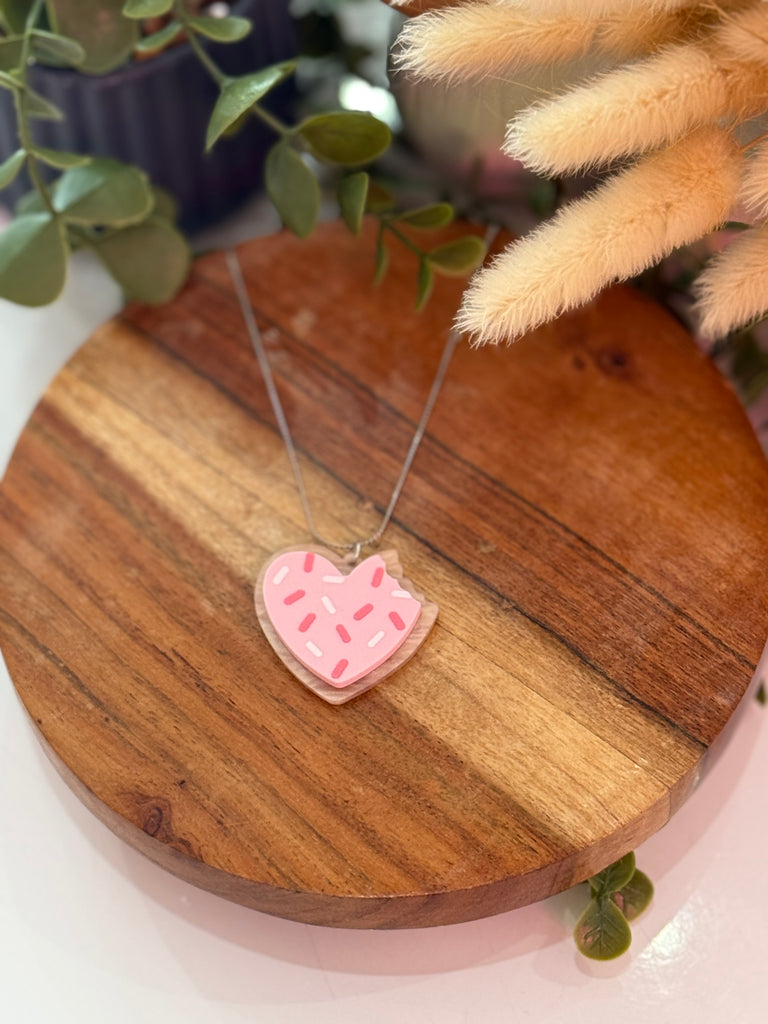 Close-up of Ellevera’s Pink Heart Cookie Necklace with pink icing and sprinkles on a silver chain.