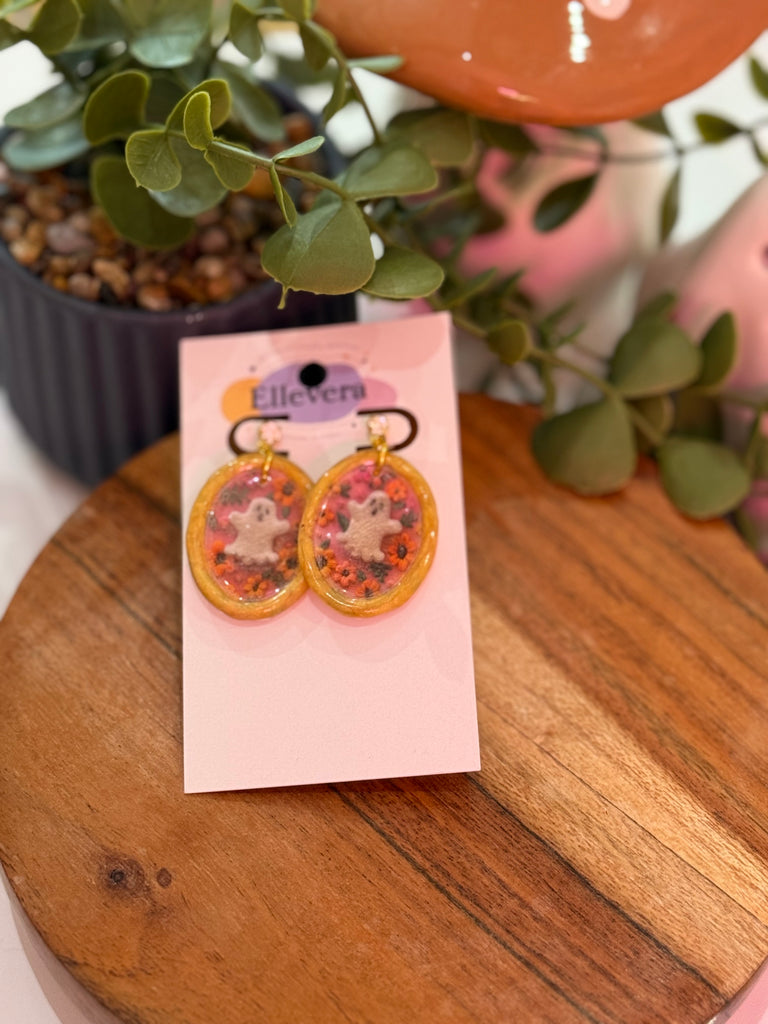 Polymer clay oval earrings with white ghost and floral details in orange and pink on Ellevera card.