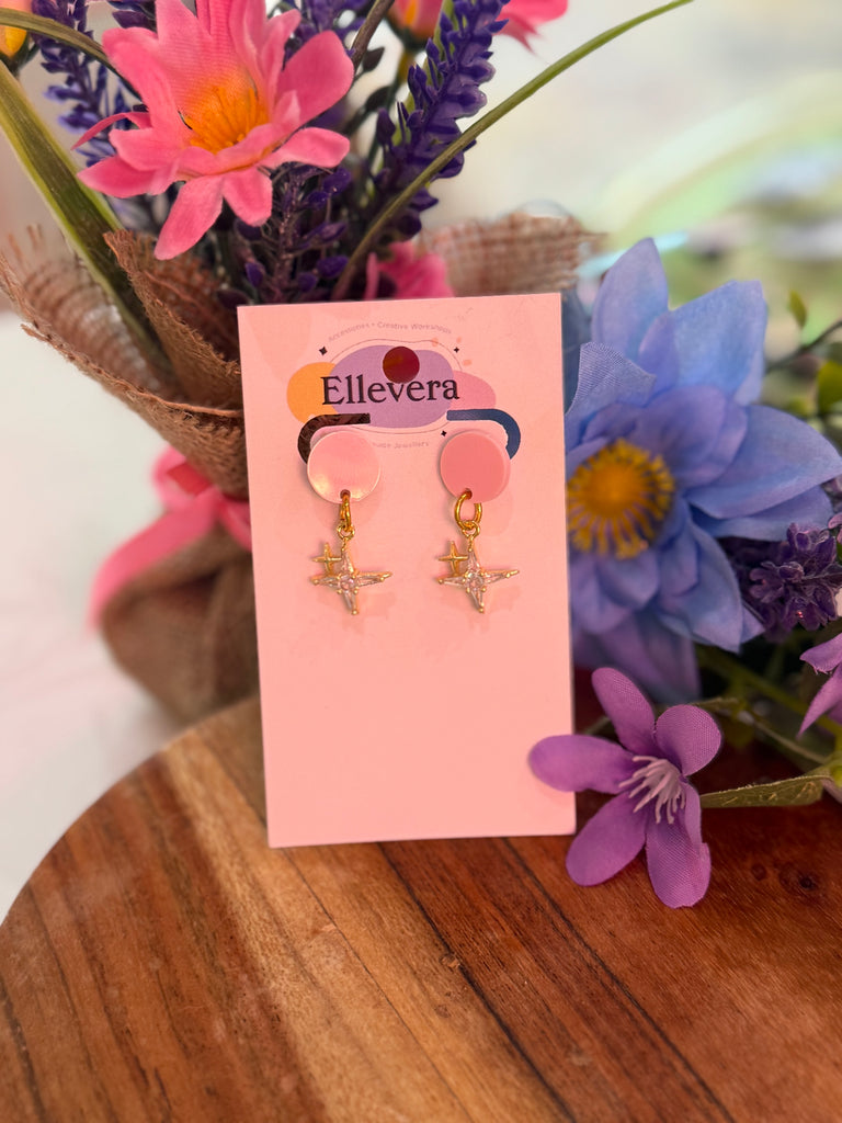 Pink acrylic stud earrings with dangling gold star charms on Ellevera backing card.