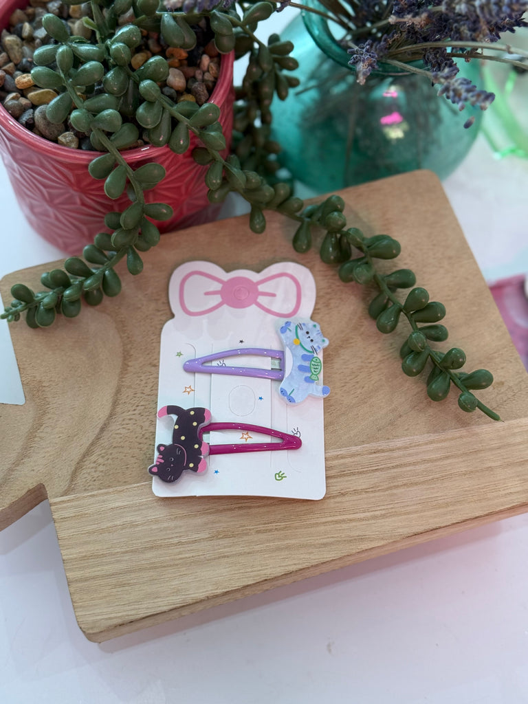 Hair clip set with black cat and blue cat designs on purple and red snap clips.