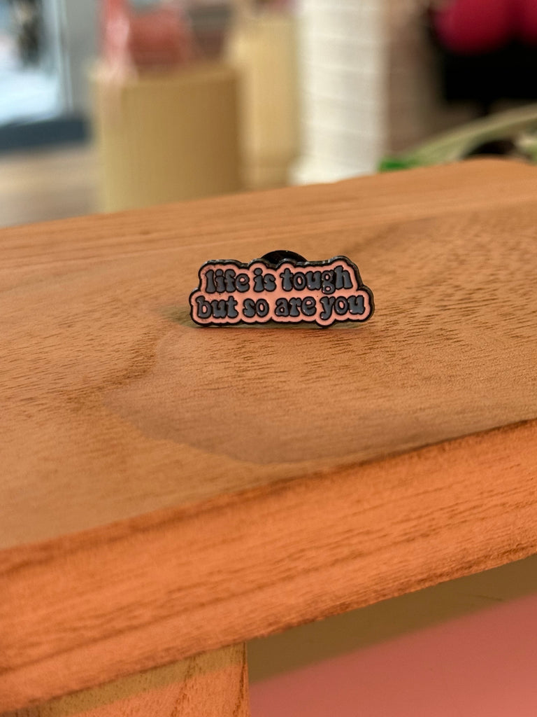 Enamel pin with the phrase "Life is tough but so are you" in bold pink and black design.