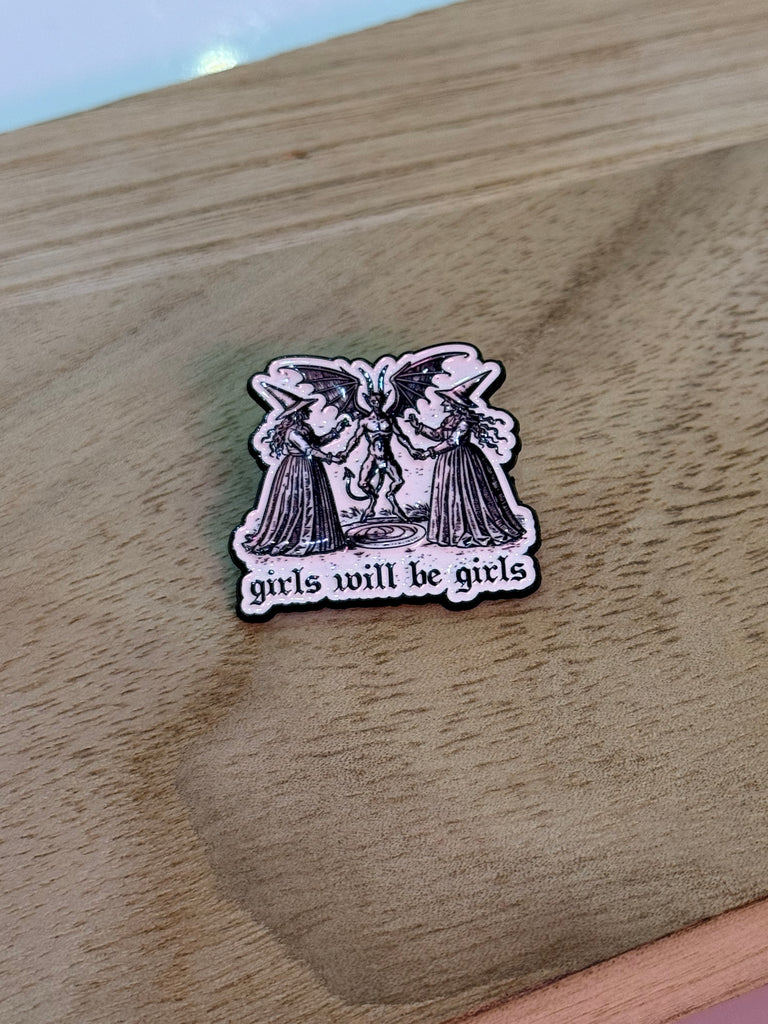 Enamel pin with phrase "Girls Will Be Girls" and gothic illustration of mystical women with a winged figure.