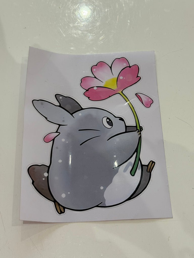 Grey bunny holding a pink flower sticker in Studio Ghibli–inspired style.